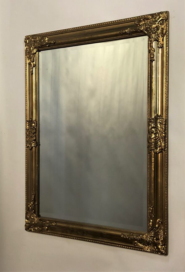 Spogulis ar dekoratīvu zelta rāmi.